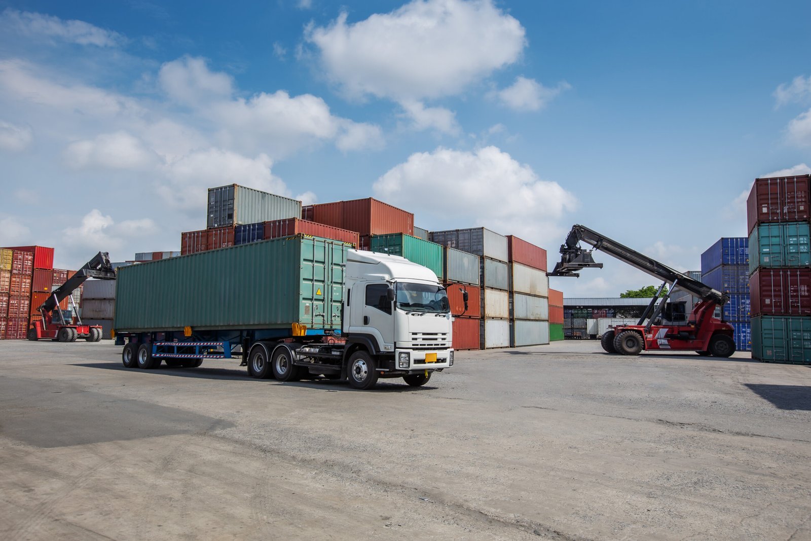 A red container forklift loads a cargo container onto a white truck in a busy shipping yard. Surrounded by stacked containers, the scene represents global logistics, trade, and freight transportation.